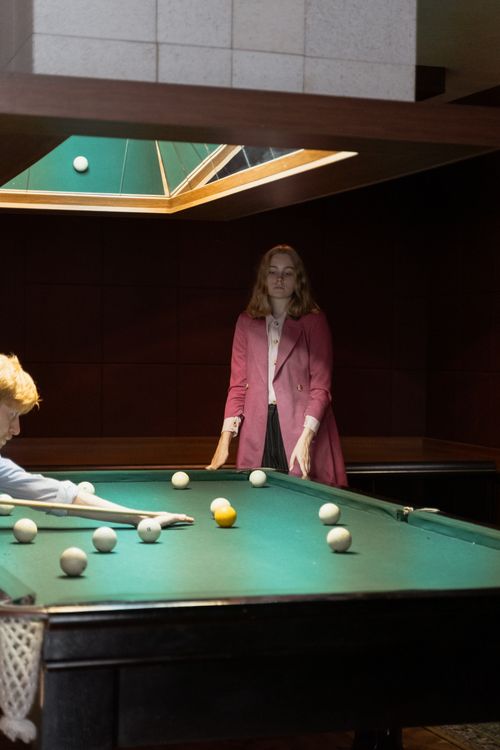 Free A woman in a pink jacket plays billiards indoors. Atmosphere is focused and dimly lit. Stock Photo