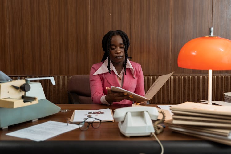 A Woman In Pink Blazer Sitting On A Swivel Chair While Reading Documents