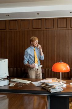 Businessman talking on phone in a vintage styled office workspace, with warm lighting.