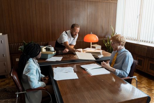 Retro office meeting with diverse team discussing documents. Mid-century style.