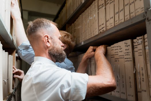 Two men organizing paperwork in an archive, focused on meticulous documentation.