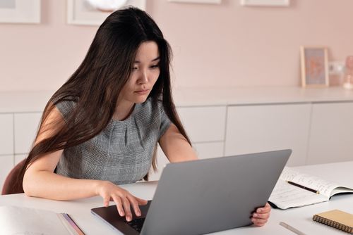 Free Asian woman in a modern office setting working on a laptop, symbolizing entrepreneurship and professionalism. Stock Photo