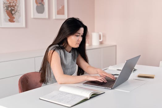 Asian woman focused on laptop work while sitting at a home office desk.