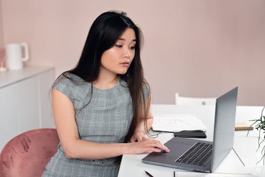 Young Asian woman working on a laptop at a modern desk, focused on a task.