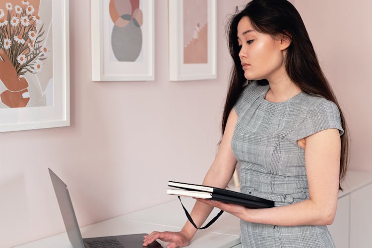 A Person Using Laptop While Holding Document