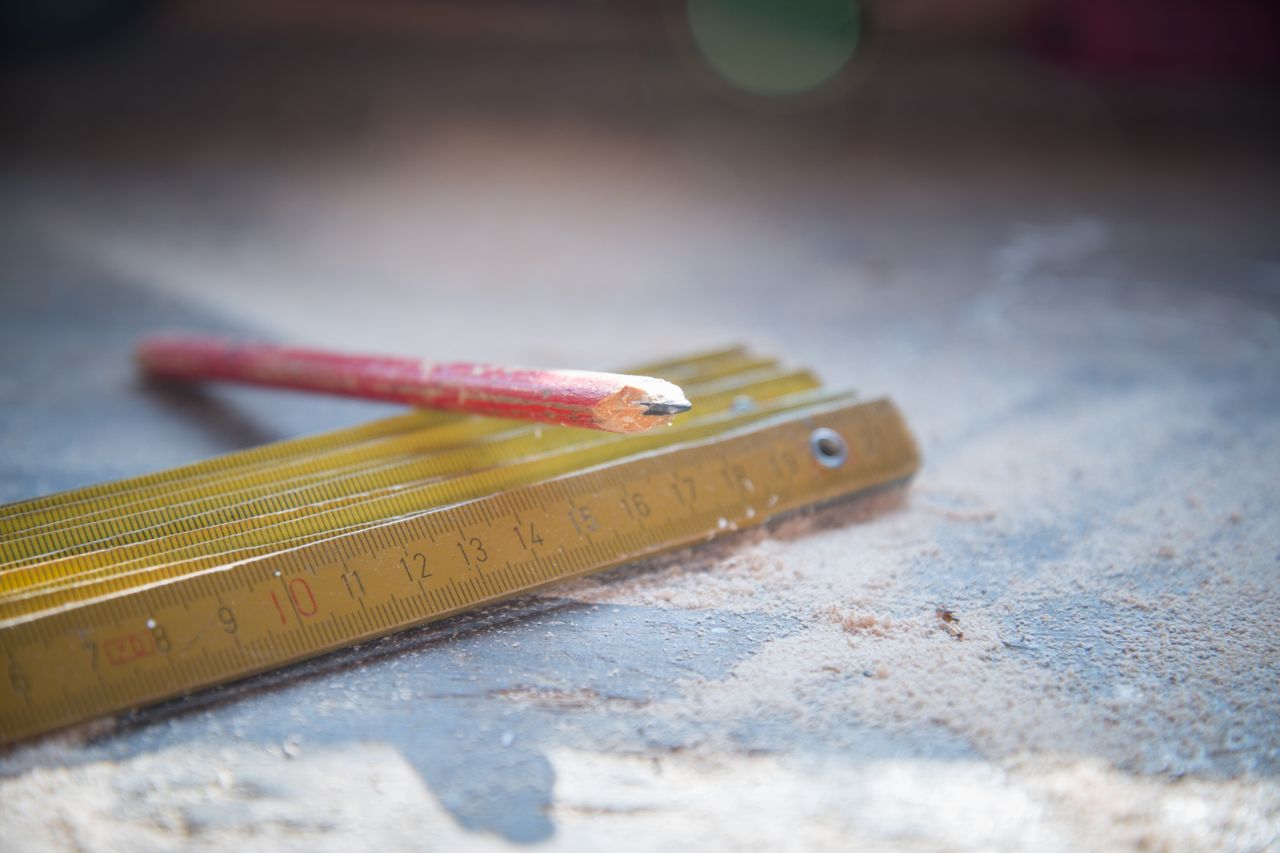 A red pencil and folding ruler on a dusty workshop table, symbolizing craftsmanship.