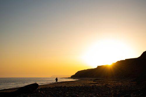 Free A beautiful beach view with silhouetted figure at sunset, highlighting cliffs and ocean. Stock Photo