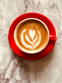 Artistic coffee latte with intricate design in a vibrant red cup on marble background.