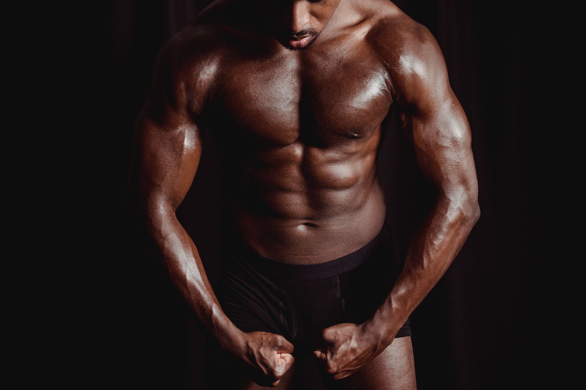 健美訓練提升自信:從新手到自我肯定的實用步驟 Athletic male bodybuilder flexing muscles in a dramatic studio setting, showcasing strength and physique.