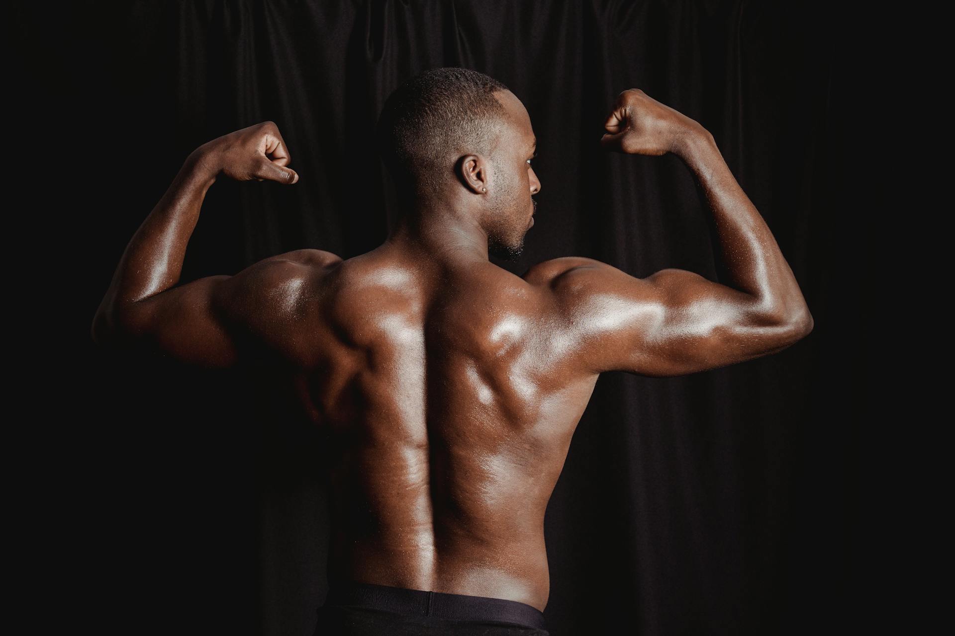 Muscular black adult male flexing back muscles against a dark backdrop, showcasing strength and fitness.