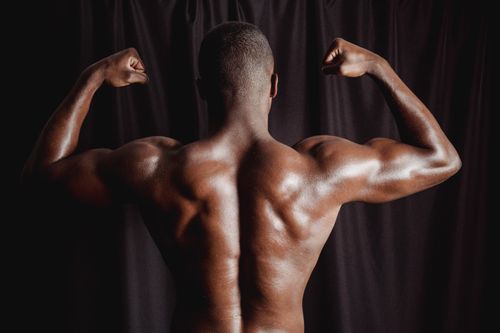 Free Back view of a shirtless man flexing his muscular arms and torso against a dark background. Stock Photo