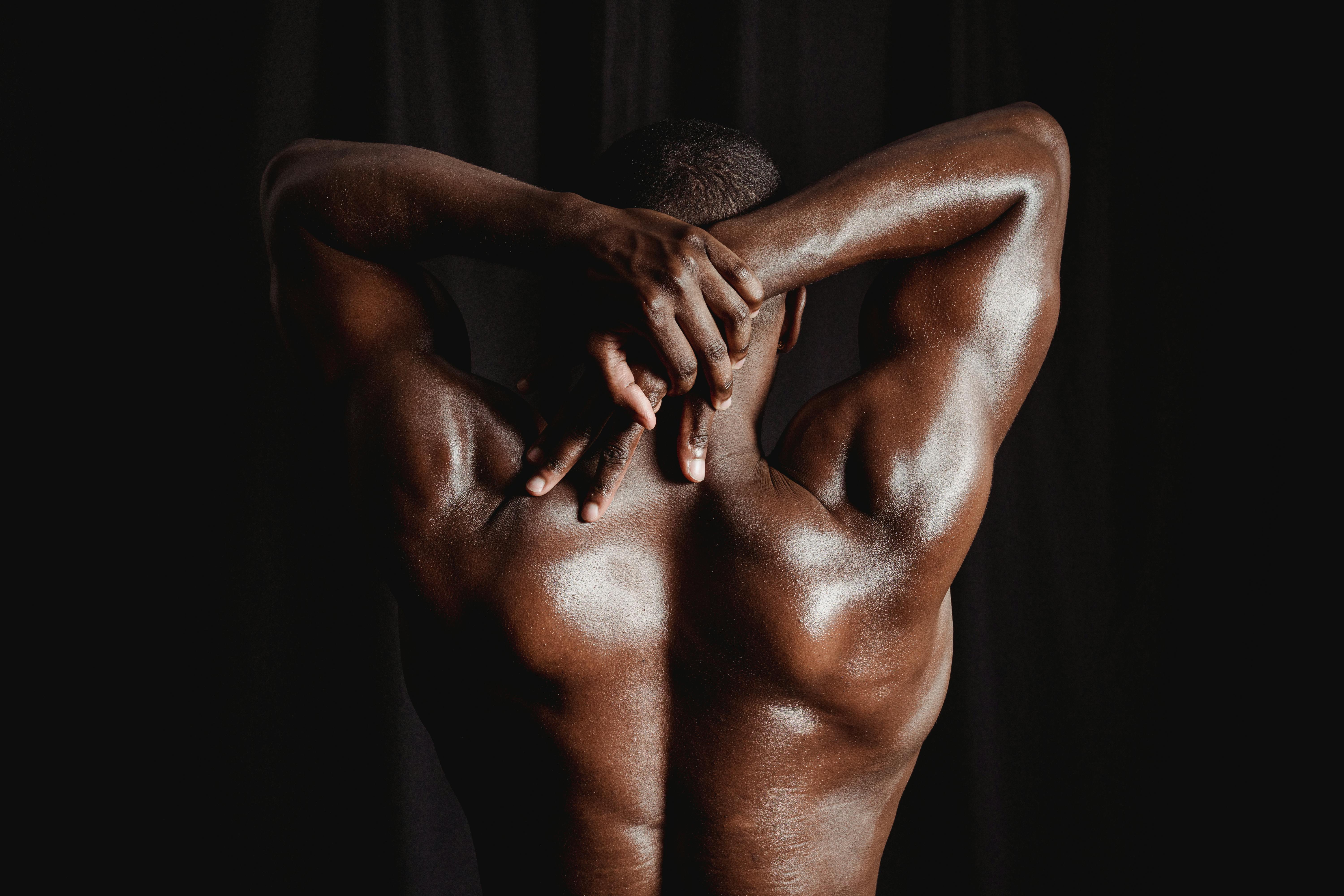Strong men with defined muscles stretching his back and arms against a dark background.