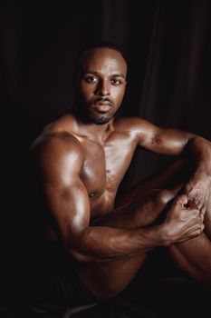 A muscular man poses shirtless against a dark background, showcasing fitness and strength.