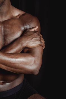Close-up of a shirtless black man showcasing muscular arms and torso in a dark setting.