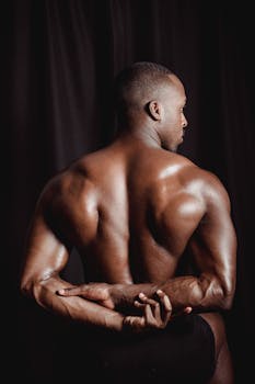 A fit black man flexes his muscular back, showcasing strength and fitness.