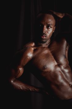 Portrait of a strong, shirtless male bodybuilder flexing muscles in a dark setting.