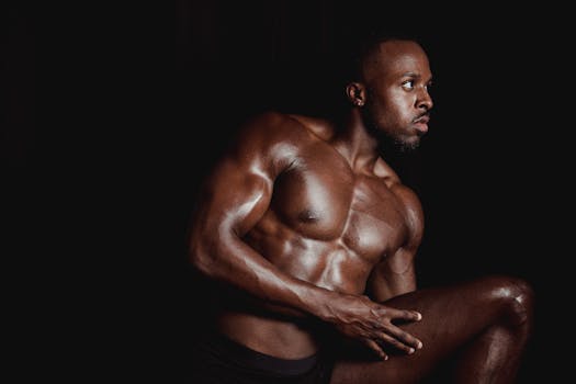 A muscled man poses topless against a dark background, showcasing fitness and strength.