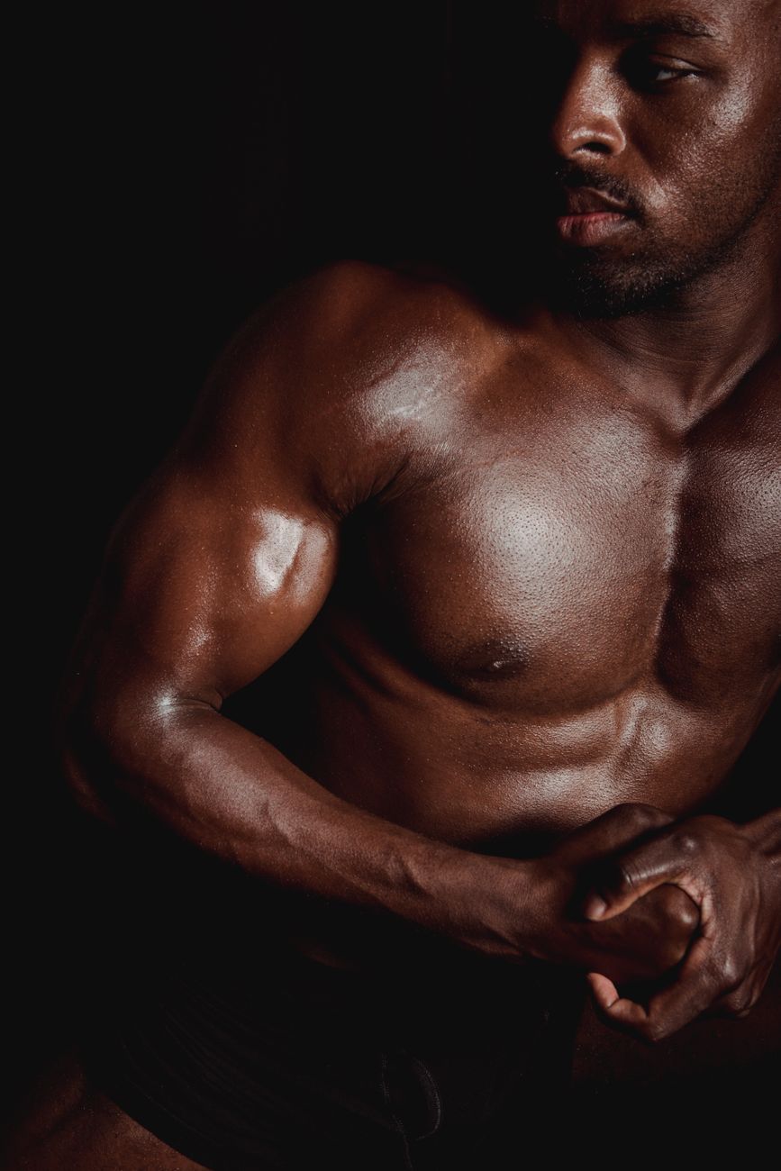 Close-up of a muscular man showcasing fit physique in a dark setting.