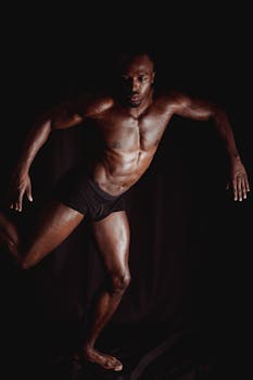 Shirtless muscular man in boxer shorts striking a dynamic pose against a dark background.