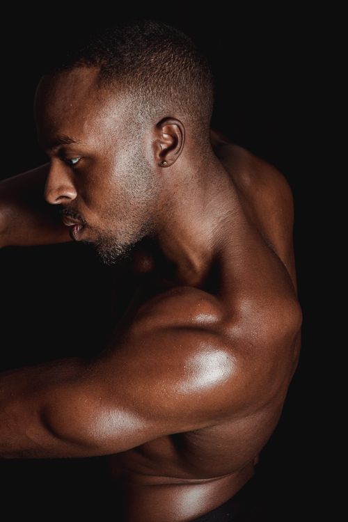 Free Shirtless muscular man posing in dramatic lighting against a dark background. Stock Photo