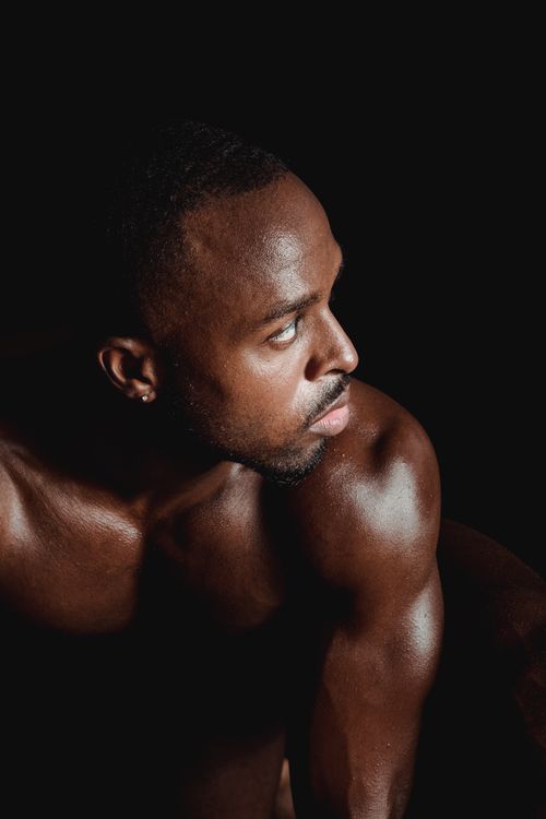 Free Muscular man posing in a dark studio setting, showcasing strength and determination. Stock Photo