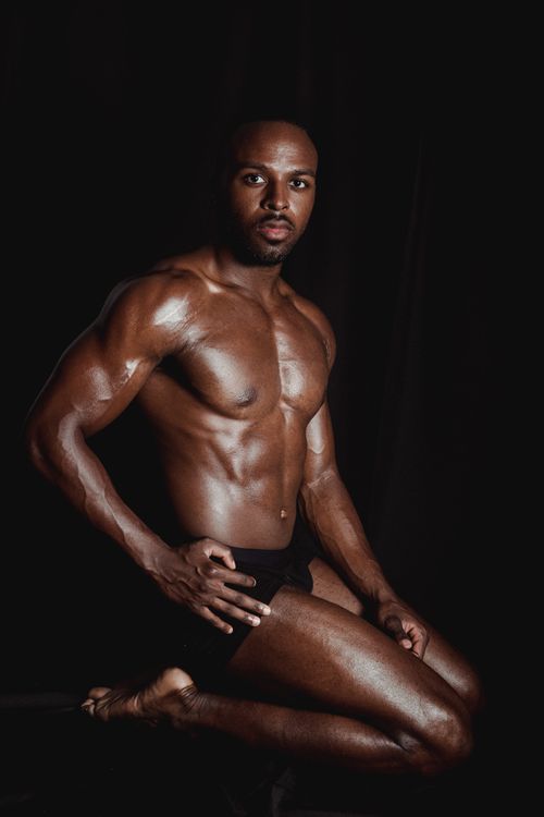 Free Studio shot of a muscular, shirtless man kneeling on a black background, showcasing strength and fitness. Stock Photo