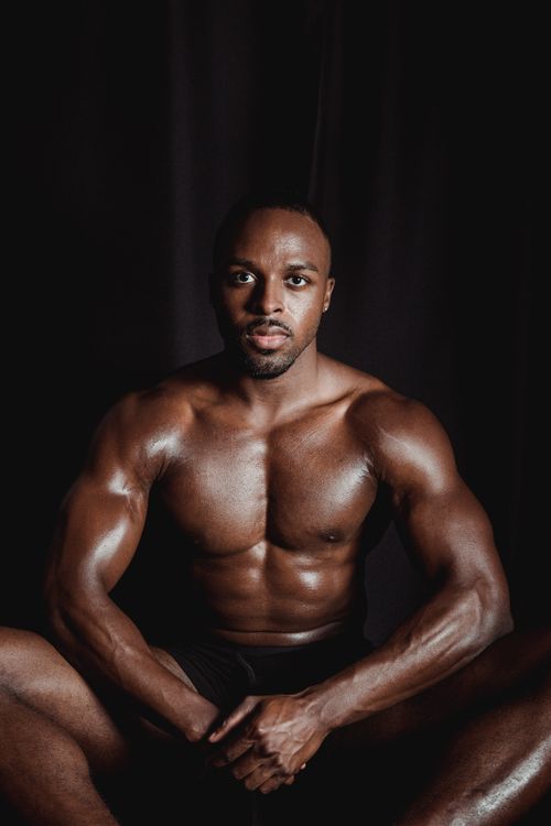 Free Dynamic portrait of a muscular man posing against a dark background, exuding strength and masculinity. Stock Photo