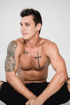 Shirtless man with tattoos posing against a white background, showcasing fitness and style.