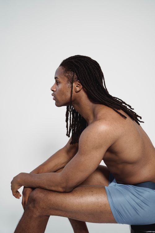 Free A shirtless man with dreadlocks poses sideways against a white background in a studio shoot. Stock Photo