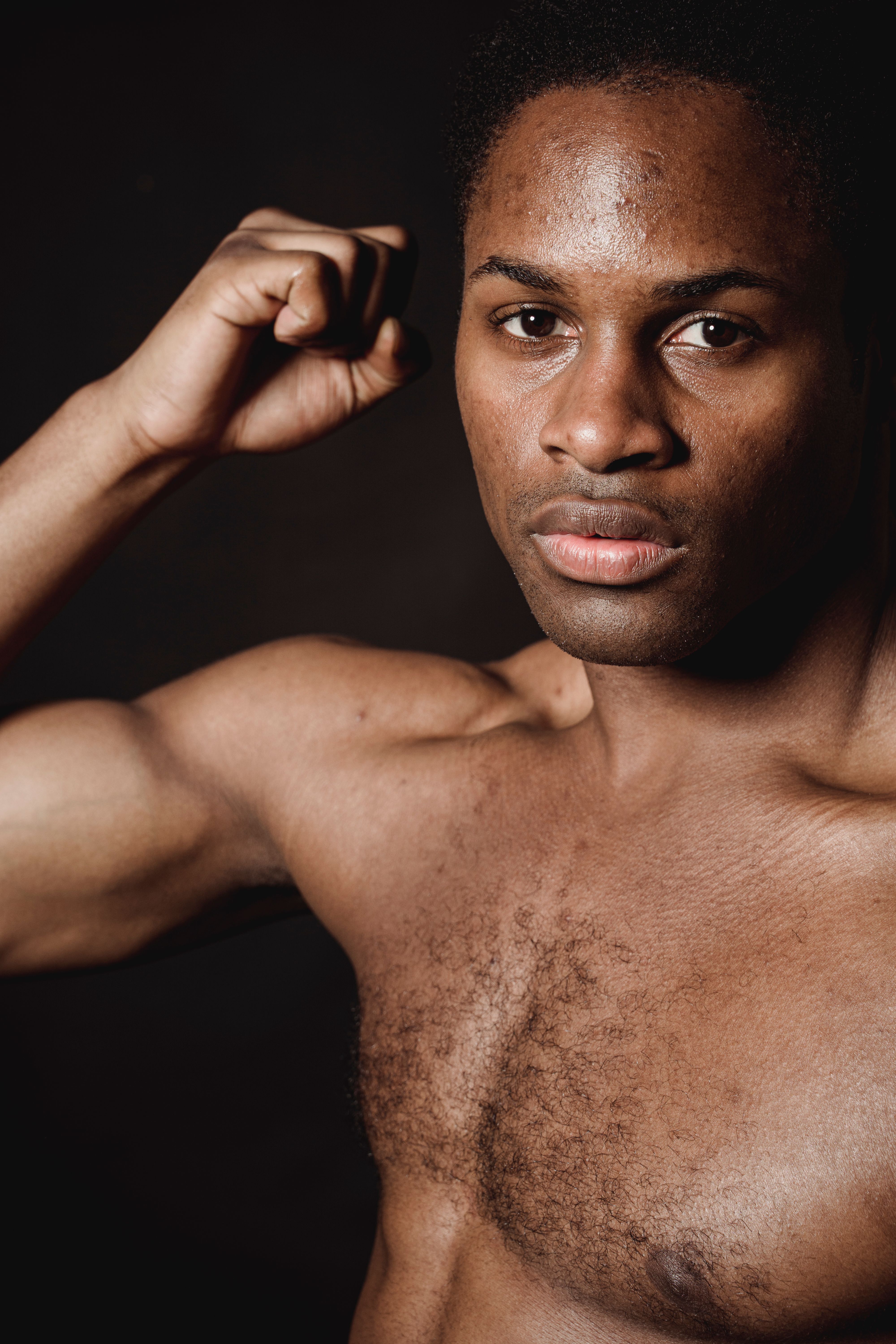 A close-up portrait of a shirtless man flexing his arm against a dark background.