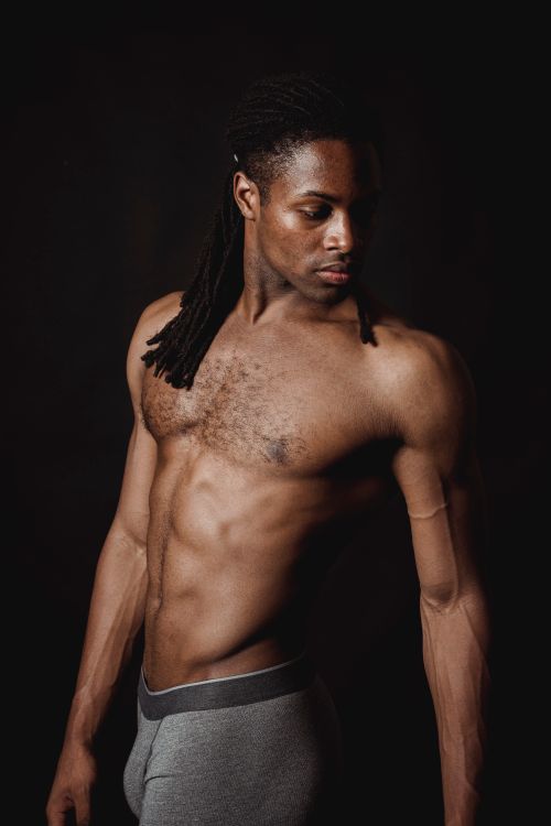 Free A muscular, shirtless man with dreadlocks poses against a black background in a studio setting. Stock Photo