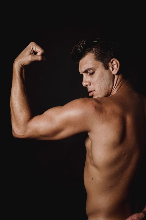 Free A shirtless muscular man flexes his bicep against a black background in a studio shoot. Stock Photo