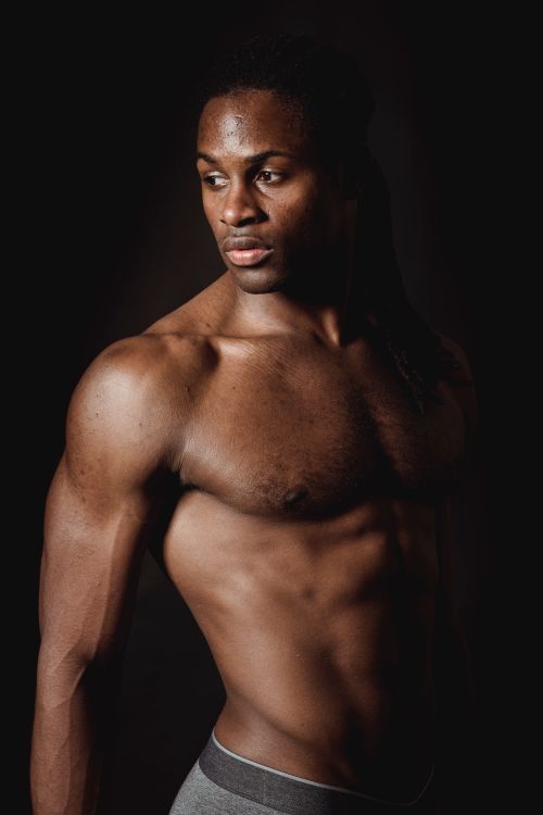 Free Shirtless African American man showing muscular physique against black background in a studio. Stock Photo