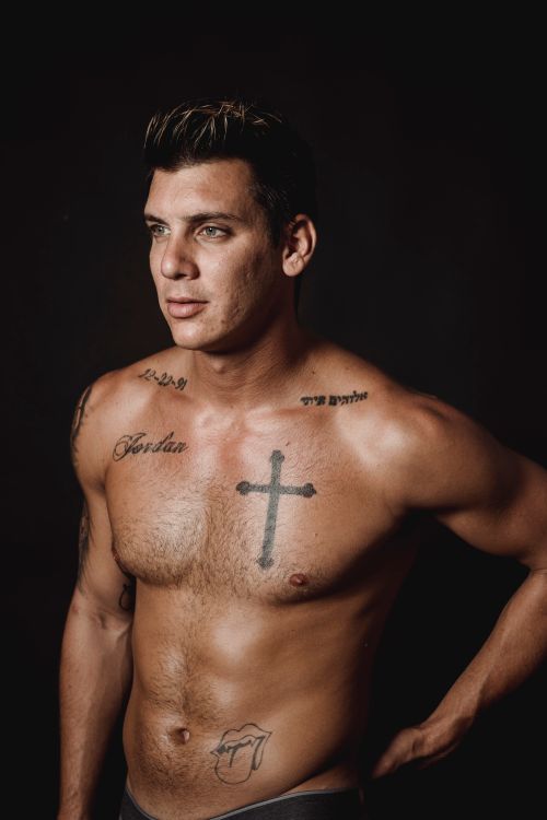 Free Portrait of a fit, tattooed, shirtless man against a black background in a studio. Stock Photo