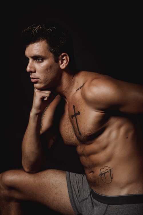 Free Shirtless muscular man with tattoos posing against dark background in studio. Stock Photo