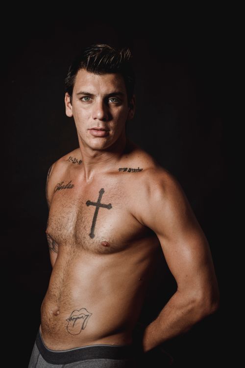 Free Shirtless tattooed man posing in a studio with a black background showcasing strength. Stock Photo