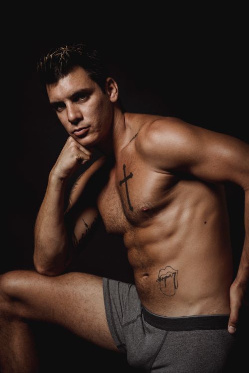Free A muscular tattooed man posing shirtless in a studio with a dark background. Stock Photo