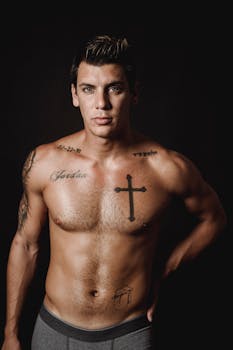Muscular tattooed man posing shirtless in a studio with a black background.