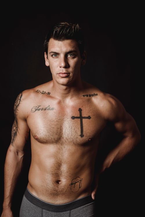 Free Muscular tattooed man posing shirtless in a studio with a black background. Stock Photo