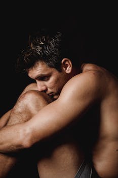 Portrait of a muscular man in a thoughtful pose against a black background.