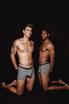 Two muscular men posing shirtless in a studio on a dark background.