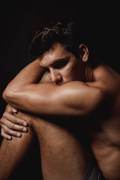 Free Dramatic portrait of a shirtless man sitting, deep in thought, in a studio setting. Stock Photo