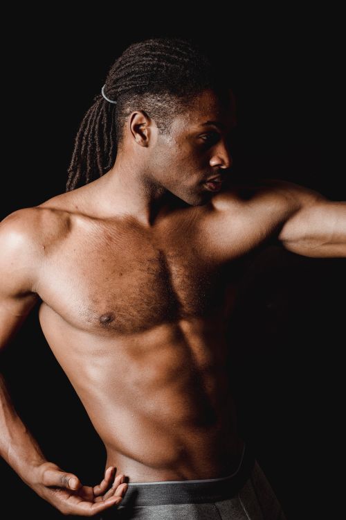 Free A shirtless black man with muscular build poses against a black background, showcasing strength and elegance. Stock Photo