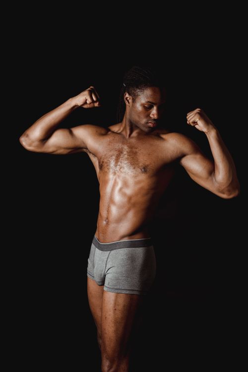 Free A muscular man flexing his biceps during a studio shoot against a black background. Stock Photo