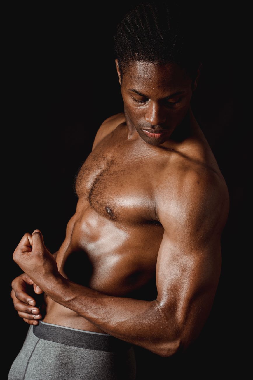 Studio shot of a shirtless muscular black man flexing against a dark background.