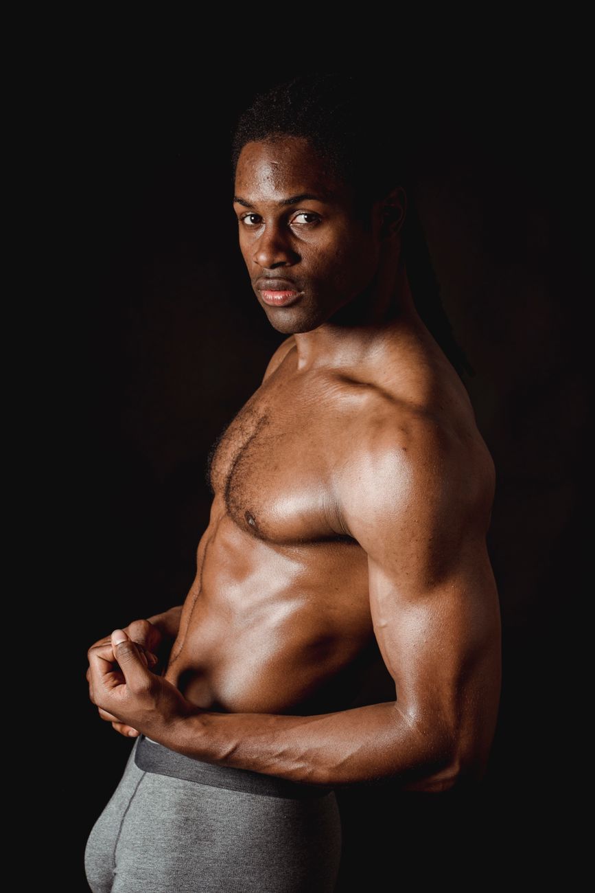 Portrait of a muscled man posing shirtless, showing off his physique against a dark backdrop.