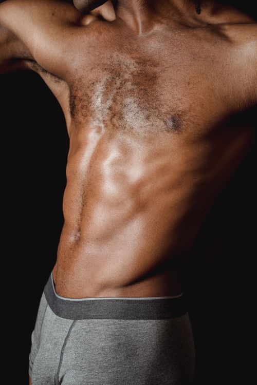 Free Close-up image of a muscular male torso with defined abs, shot on a black background. Stock Photo