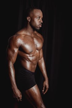 Shirtless muscular man posing in profile against a dark background. Fitness and strength concept.
