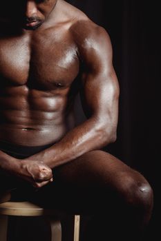 Close-up of a shirtless muscular man sitting, showcasing defined muscles and athletic build.