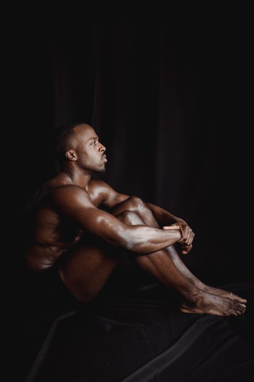 Free Striking portrait of a man sitting shirtless on a dark background in a studio setting. Stock Photo